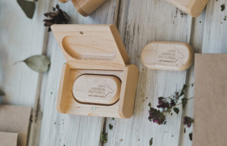 Bild: Auf diesem Foto sind zwei hölzerne ovalförmige USB-Sticks zu sehen, einer davon in einem Holz-Etui. Darauf eingraviert befinden sich schlicht das Logo der Tierfotografin Lira Amarok, sowie ihre Webadresse.