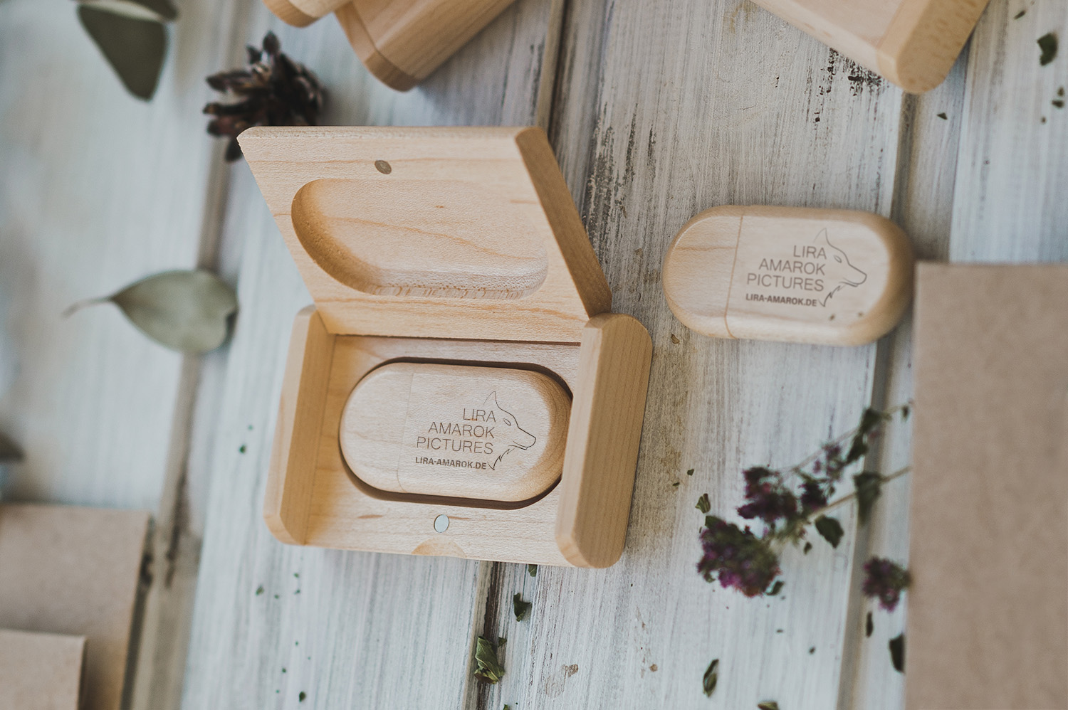 Bild: Auf diesem Foto sind zwei hölzerne ovalförmige USB-Sticks zu sehen, einer davon in einem Holz-Etui. Darauf eingraviert befinden sich schlicht das Logo der Tierfotografin Lira Amarok, sowie ihre Webadresse.
