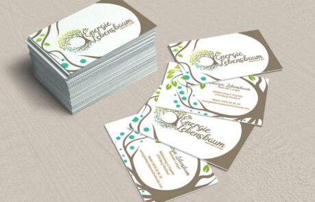Bild: Ein Stapel Visitenkarten sowie 4 ausgefächerte Visitenkarten die Front- und Rückseite des Logobasierten Designs von Energie Lebensbaum zeigen. Hierbei rahmt der im Logo verwendete Lebensbaum die Inhalte der Visitenkarte ein.